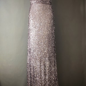May include: A long, sleeveless, sequined dress in a rose gold color. The dress has a simple, square neckline and a fitted silhouette.