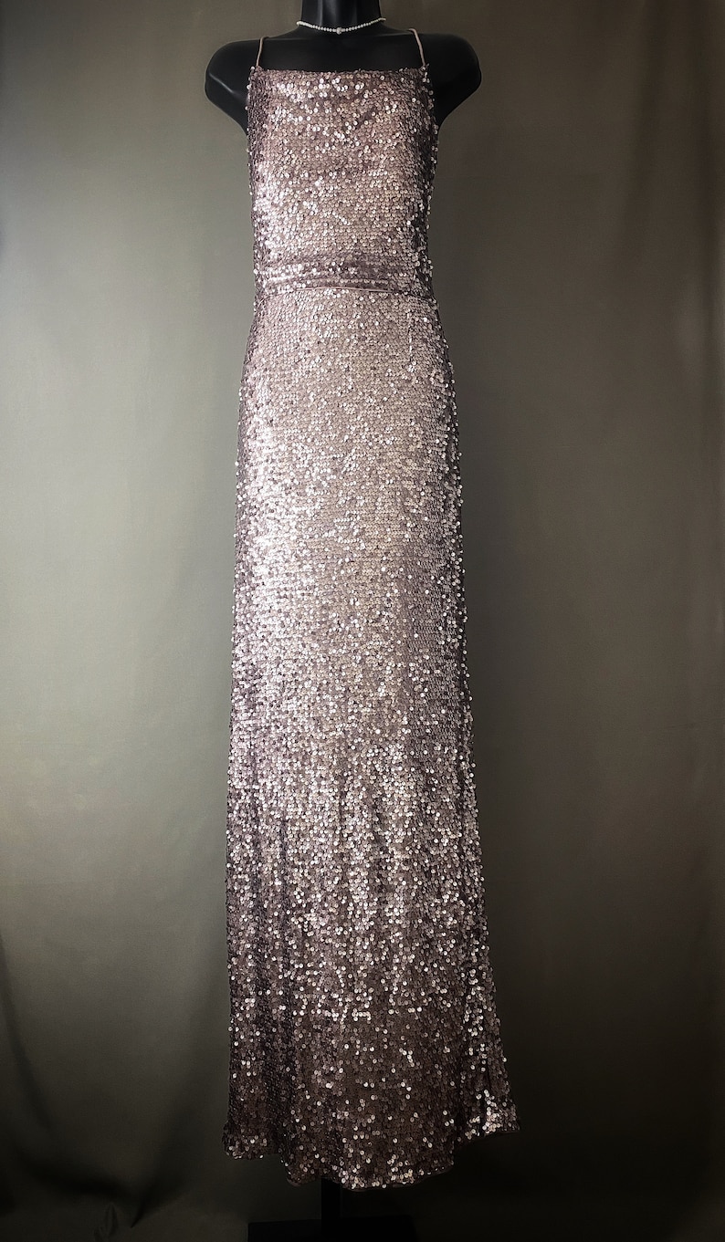 May include: A long, sleeveless, sequined dress in a rose gold color. The dress has a simple, square neckline and a fitted silhouette.