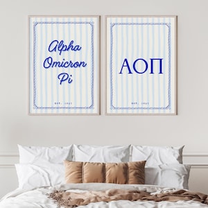 May include: Two framed prints with blue and white striped backgrounds. The left print says "Alpha Omicron Pi" in blue script, and the right print says "AOP" in blue capital letters. Both prints have a decorative blue border and the text "Est. 1897".