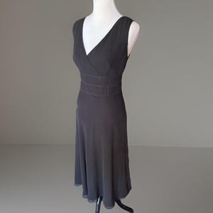 Puede incluir: Un vestido sin mangas gris oscuro con cuello en V y cintura entallada. El vestido se exhibe en un maniqu&iacute; blanco sobre un fondo gris. La falda se ensancha desde la cintura, creando una silueta fluida.