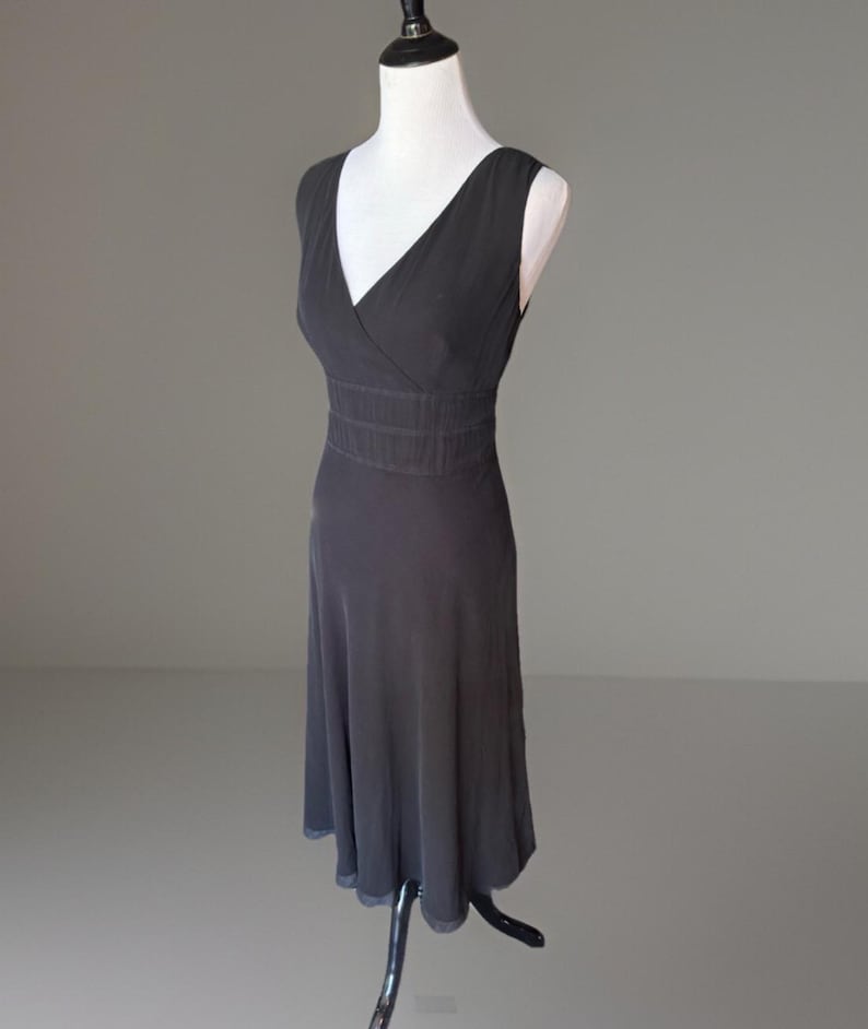 Puede incluir: Un vestido sin mangas gris oscuro con cuello en V y cintura entallada. El vestido se exhibe en un maniqu&iacute; blanco sobre un fondo gris. La falda se ensancha desde la cintura, creando una silueta fluida.