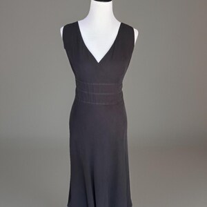 Puede incluir: Un vestido negro sin mangas con cuello en V y cintura entallada. El vestido se exhibe en un maniqu&iacute; blanco sobre un fondo gris. La falda se ensancha ligeramente desde la cintura.