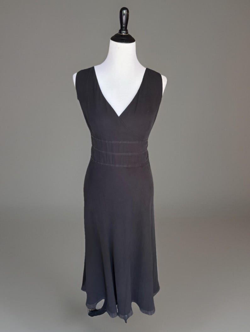 Puede incluir: Un vestido negro sin mangas con cuello en V y cintura entallada. El vestido se exhibe en un maniqu&iacute; blanco sobre un fondo gris. La falda se ensancha ligeramente desde la cintura.