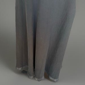 Puede incluir: Un vestido largo y fluido en un tono gris apagado. La tela cae en suaves pliegues, con un brillo sutil. El dobladillo est&aacute; terminado con un ribete plateado, agregando un toque de elegancia al dise&ntilde;o simple. Ideal para eventos.
