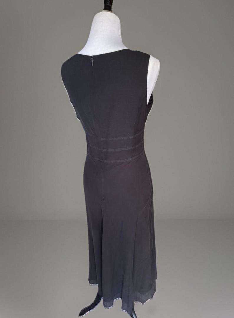 Puede incluir: Vestido sin mangas, gris oscuro, exhibido en un maniqu&iacute;. El vestido presenta un escote en V, una cintura entallada con detalles horizontales y una falda fluida. El dobladillo est&aacute; rematado con un ribete decorativo.