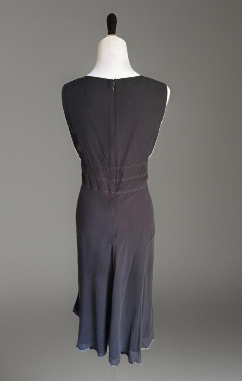Puede incluir: Vestido negro sin mangas exhibido en un maniqu&iacute;. El vestido presenta un escote en V, una cintura entallada con costuras horizontales y una falda fluida que llega hasta la pantorrilla. El vestido tiene cierre de cremallera en la espalda.
