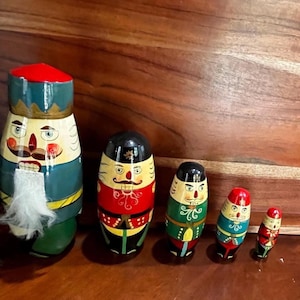 May include: A set of six wooden nutcracker dolls in various sizes. The dolls are painted with detailed faces, uniforms, and hats in red, green, blue, and black. The largest doll has a white beard and holds a silver sword.