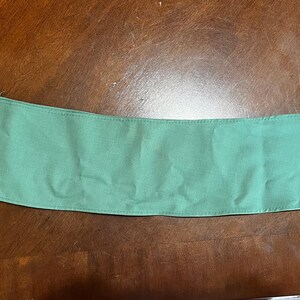 May include: A seafoam green fabric collar, likely for a garment, lies on a brown wooden surface. The collar is rectangular with a pointed end, and appears to be made of a soft, woven material. The item is a solid color.
