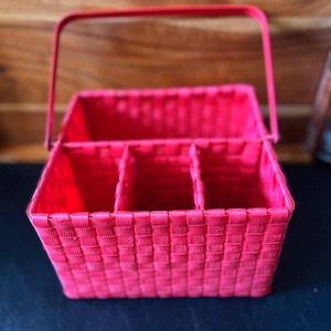 May include: A bright red rectangular woven basket featuring a sturdy matching handle and three internal compartments. The basket is constructed from a uniform woven material with a consistent grid pattern throughout the base and sides.