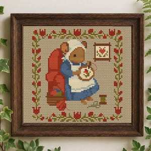 May include: Cross-stitch artwork in a dark wood frame. The image depicts a mouse in a blue dress and white bonnet, cross-stitching. A red chair and floral border surround the scene. A small framed heart hangs on the wall.
