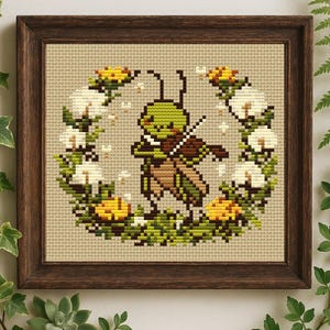 May include: A cross-stitch embroidery in a dark brown wooden frame featuring a green grasshopper playing a brown violin. The grasshopper is centered within a circular wreath composed of white cotton-like flowers, yellow blossoms, and green leaves.