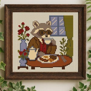 May include: Cross-stitch artwork in a dark wooden frame. The image depicts a raccoon wearing sunglasses, seated at a table with a cup, teapot, and plate of food. A vase of red roses and a window are also visible.