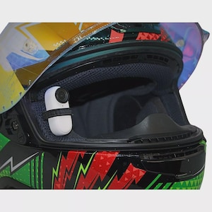 May include: A black motorcycle helmet with a green, red, and white graphic design. A small white camera is mounted on the inside of the helmet.