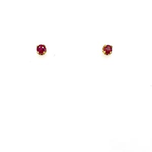 May include: A pair of stud earrings featuring small, round, faceted red gemstones set in gold metal prongs. Each earring consists of a single circular stone held securely by a simple metal setting, designed to be worn as a classic, minimalist accessory.