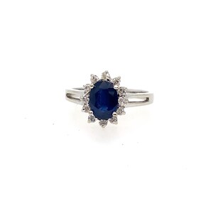 May include: A silver-toned ring featuring a central oval-cut deep blue sapphire gemstone. The sapphire is surrounded by a halo of small, clear, round-cut white stones. The band is made of a polished metallic material and has a split-shank design.