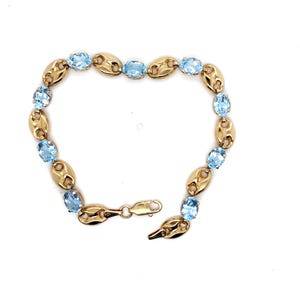 May include: A gold link bracelet featuring alternating oval-shaped light blue gemstones and polished gold coffee bean-style links. The bracelet is secured with a lobster claw clasp and includes a small metal tag marked with the text 10K.