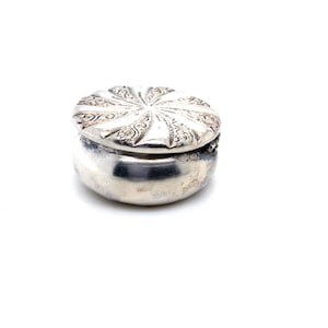 May include: A silver trinket box with an ornate, swirling design on the lid. The box is closed and has a rounded shape.