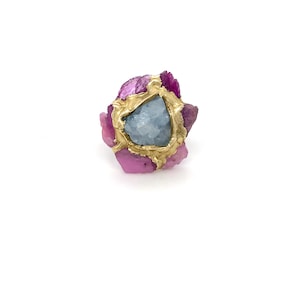 May include: A gold ring with a blue gemstone surrounded by pink crystals.