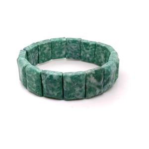 May include: A green and white stone bracelet. The bracelet is made of rectangular, polished stones strung together to form a flexible band. The stones have a mottled pattern of green and white, creating a natural, organic look. The bracelet is shown against a white background.
