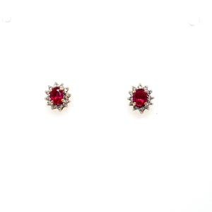 May include: A pair of stud earrings featuring oval-cut red gemstones at the center, each surrounded by a halo of small, clear, sparkling stones set in a metallic frame with a post backing for secure attachment to the earlobe.