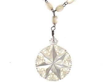 Puede incluir: Un collar de perlas blancas con un colgante de estrella blanca tallada. El colgante está unido al collar con un alambre de plata.
