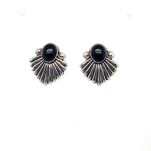 May include: A pair of silver earrings featuring a central oval black stone set within a fan-shaped metal base. The design includes radiating fluted lines and small spherical accents at the top corners, creating a symmetrical, polished appearance.