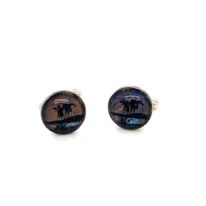 May include: A pair of silver cufflinks with round, black, resin-like settings. Each setting features a colorful butterfly wing pattern with a silhouette of three palm trees.
