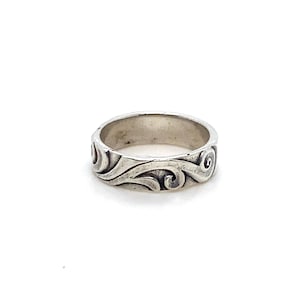 May include: A silver ring with a swirling, wave-like pattern. The ring has a wide band and a detailed design that wraps around the entire circumference. The ring is set against a white background.