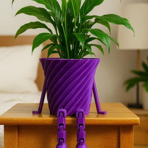 May include: A purple, 3D-printed planter with a spiral design, holding a green plant with large leaves and a white flower. The planter has legs and feet, giving it a whimsical appearance. The planter is sitting on a wooden table.