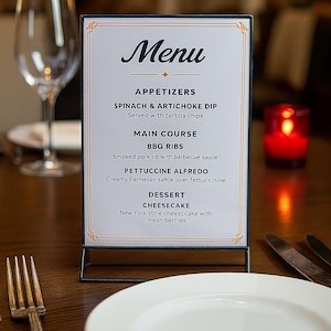 May include: A restaurant menu displayed on a table. The menu features appetizers, main courses like BBQ ribs, and desserts such as cheesecake. The menu is in a black metal frame with a decorative border.