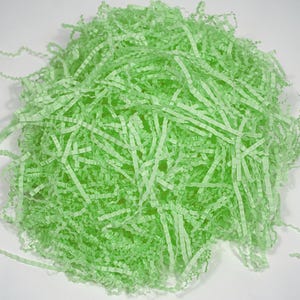 May include: A pile of light green crinkle paper, ideal for gift packaging or basket filler. The shredded paper has a textured, wavy appearance, and is arranged in a loose, irregular shape against a white background.