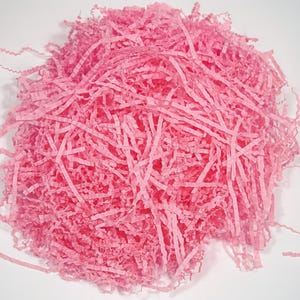 May include: A pile of pink shredded paper, ideal for gift packaging or decorative purposes. The paper is cut into thin strips, creating a textured and voluminous appearance. The color is a vibrant, eye-catching pink.