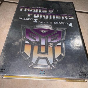 Op de afbeelding: Een dvd-hoes voor The Original Transformers Seizoen 3 Deel 2 & Seizoen 4. De hoes is zilverkleurig met een paars en zilver Transformers-logo. De tekst "TRANSFORMERS" staat bovenaan, met "SEIZOEN 3 DEEL 2 & SEIZOEN 4" eronder.