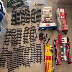 May include: A selection of toy train parts, including curved and straight tracks, carriages, and a red and silver locomotive. The train carriages have circus-themed designs and the text "ALL STAR CIRCUS".