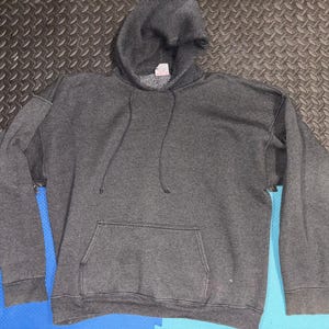 May include: A dark gray hooded sweatshirt with a front pocket and drawstring. The sweatshirt is made of a soft material and has a tag on the inside of the hood.