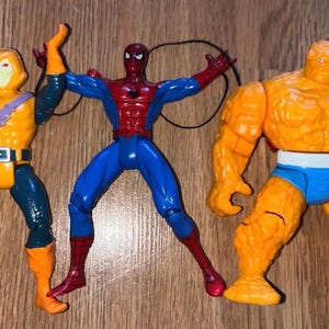以下が含まれることがあります： コミックキャラクターのアクションフィギュア3体。フィギュアには、赤と青のスーツを着たスパイダーマン、オレンジと青の衣装を着たザ・シング、オレンジとティールの衣装を着たホブゴブリンが含まれています。