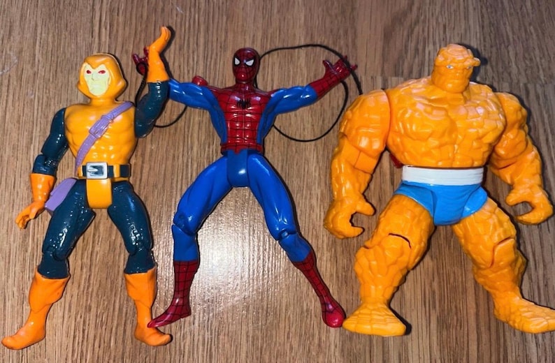 以下が含まれることがあります： コミックキャラクターのアクションフィギュア3体。フィギュアには、赤と青のスーツを着たスパイダーマン、オレンジと青の衣装を着たザ・シング、オレンジとティールの衣装を着たホブゴブリンが含まれています。