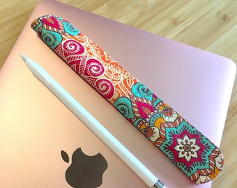 May include: A pink laptop computer with a white Apple logo and a colorful patterned pencil holder. The pencil holder has a floral design with red, orange, yellow, blue, and green colors.