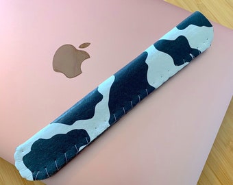 May include: A black and white cow print laptop sleeve with a pink laptop in the background.