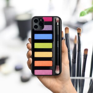 May include: Black phone case with a colorful eyeshadow palette design and a small makeup brush. The case has a clear plastic window to show the eyeshadow colors. The text "JESSICA" is printed on the brush.