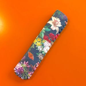 May include: A floral patterned fabric pencil case with a black background and a stitched edge.
