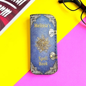 May include: A blue eyeglass case with a gold design and the text "Melissa's Spell Book".