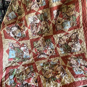 May include: A patchwork quilt with a repeating pattern of squares. The squares feature a variety of images in shades of brown, red, green, and beige. The quilt has a red border and a beige backing.