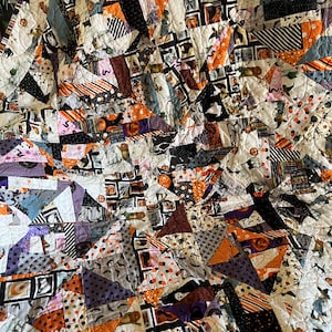 Può includere: Una trapunta di Halloween fatta a mano con un design patchwork. La trapunta presenta vari tessuti arancioni, neri, viola e bianchi, con motivi a tema Halloween come pipistrelli, zucche e fantasmi. La trapunta è cucita a macchina con un motivo trapuntato.