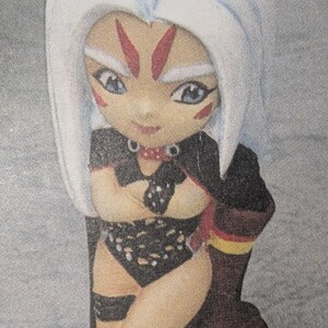 Puede incluir: Figura de cerámica de un personaje con cabello blanco, marcas rojas y ojos azules. La figura viste un atuendo negro con un cuello decorativo y está sentada sobre una base marrón con detalles amarillos. La figura tiene una apariencia estilizada y de dibujos animados.