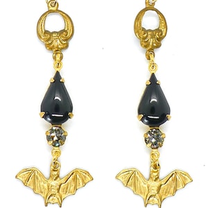 May include: Gold dangle earrings with black teardrop-shaped stones, clear rhinestones, and bat charms.