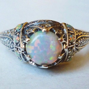 Peut inclure: Une bague en argent avec une opale sertie dans un motif de filigrane. La bague présente un motif floral délicat et est rehaussée de petites opales.