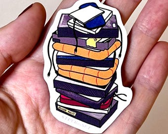 Puede incluir: Una pegatina con una pila de libros coloridos, en tonos morado, naranja y azul. Unos auriculares negros cuelgan de los libros. La pegatina incluye el texto "MURDE = STUCK-SET".