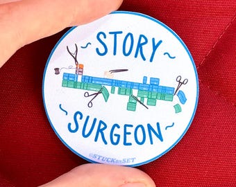Puede incluir: Una pegatina circular blanca con borde azul que presenta el texto azul STORY SURGEON. El diseño incluye ilustraciones de tiras de película azules y verdes, tijeras y un carrete de hilo. El pequeño texto STUCKONSET está impreso en la parte inferior.