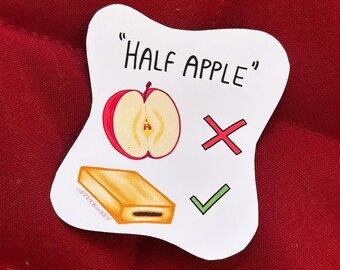 Puede incluir: Una pegatina blanca con el texto "HALF APPLE" e ilustraciones. Presenta una mitad de manzana roja y amarilla, una pastelería rectangular, una X roja y una marca de verificación verde. La pegatina tiene el texto "STICKERSET".